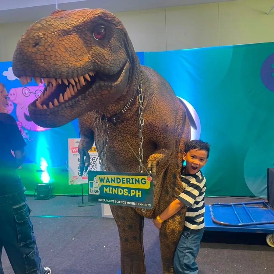 A young boy hugging the Wandering Minds Jurassic T-Rex mascot at SM Megamall