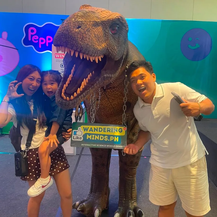 A family laughing together beside the Jurassic T-Rex mascot at the EDAMAMA New Mama Expo 2026